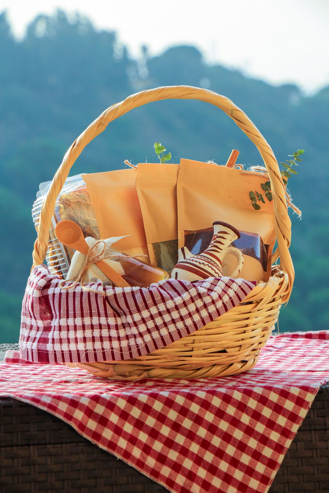 The Mounet el Téta basket on a red gingham cloth: kraft bags of zaatar and sumac, the clay jug and a jar of apple jam